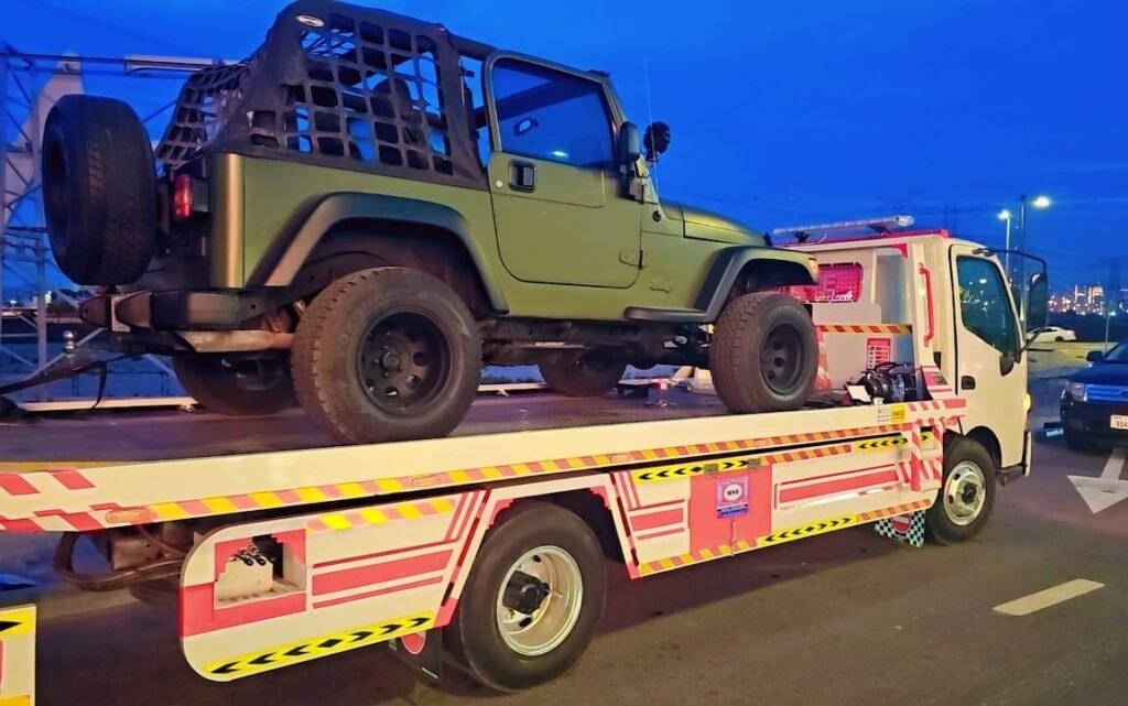 Green Jeep Wrangler on an illuminated flatbed recovery truck at night