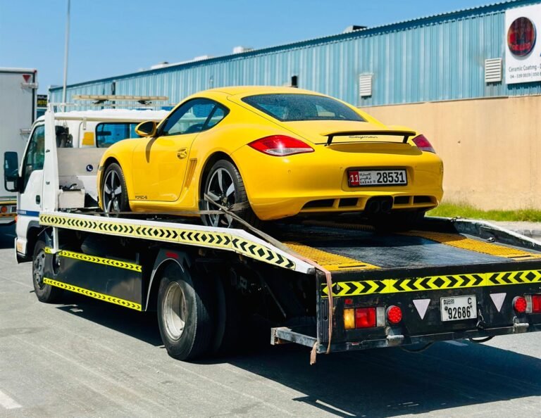 Yellow Porsche Cayman strapped onto a flatbed recovery truck in Dubai