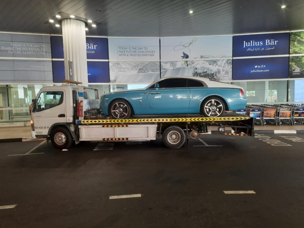 Rolls-Royce coupe carried on a flatbed truck under a covered drop-off area